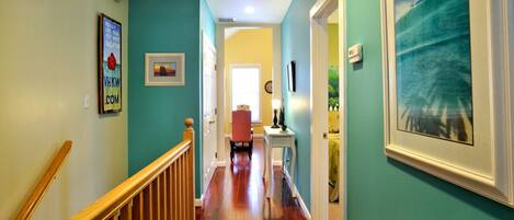 A hallway with wooden flooring, teal walls, and a framed picture of a beach scene.