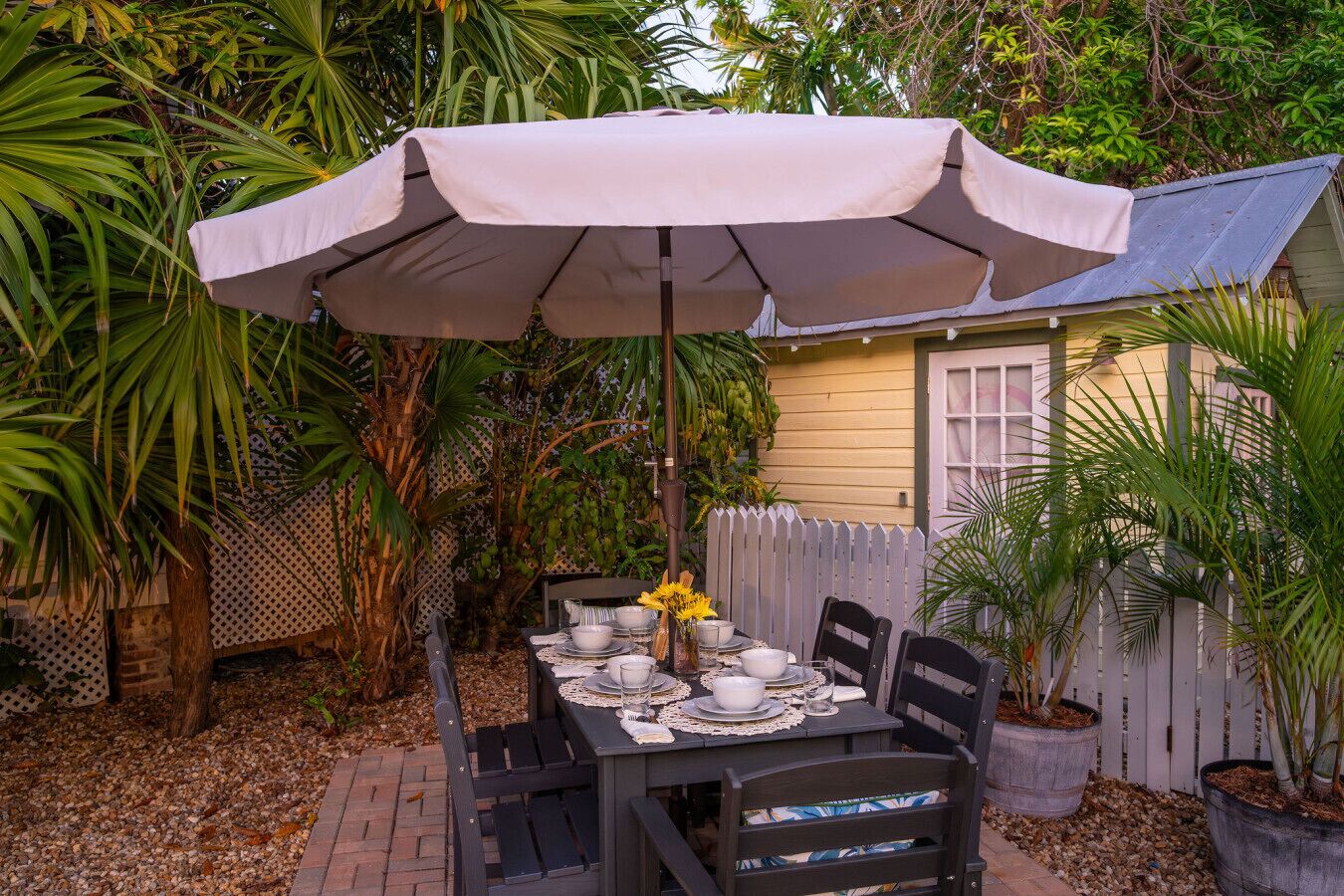An outdoor dining area with a table set for four, surrounded by chairs, under a large umbrella.