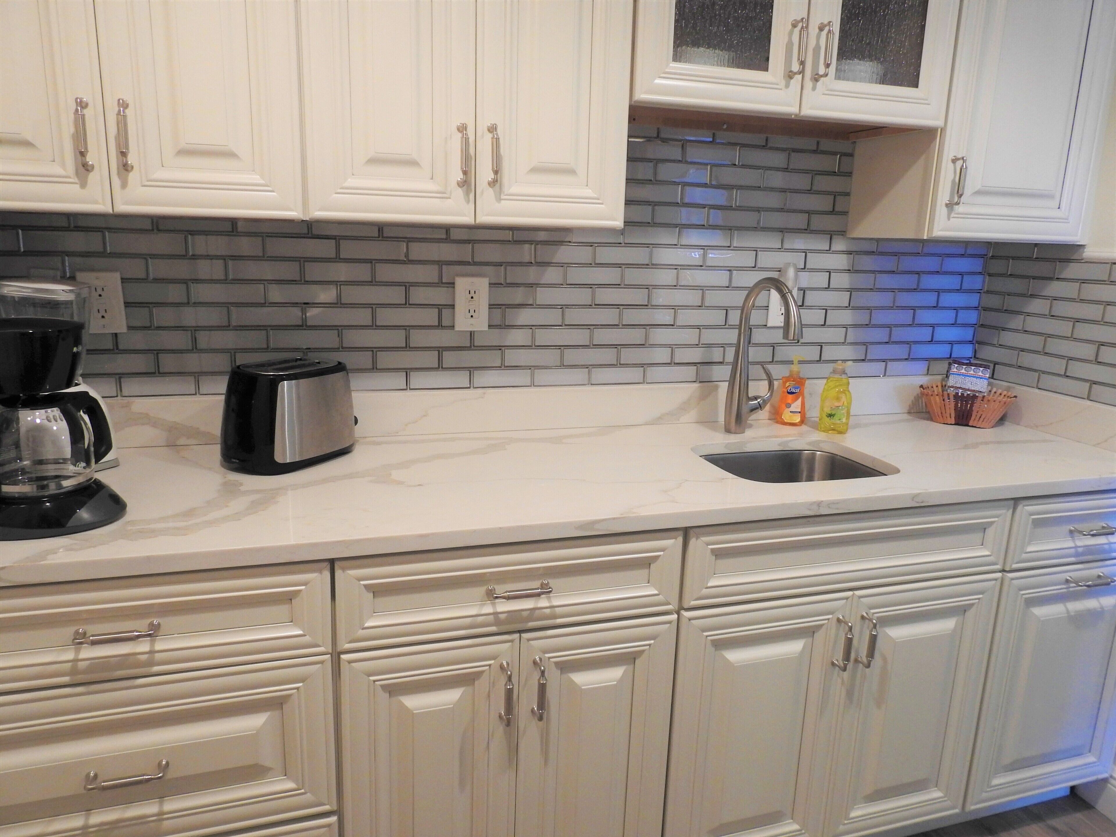 A kitchen with white cabinets, a marble countertop, a sink, and a coffee maker.