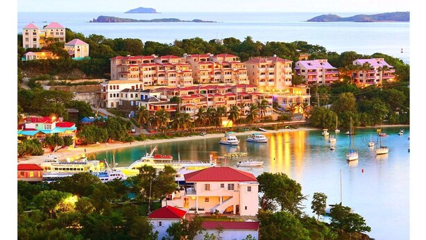 Une station balnéaire comprenant plusieurs bâtiments, un port de plaisance avec des bateaux, et offrant une vue sur la mer et les îles lointaines.