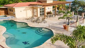 Une piscine à la forme originale, entourée de chaises longues et d’un espace patio aménagé avec des tables et des chaises.