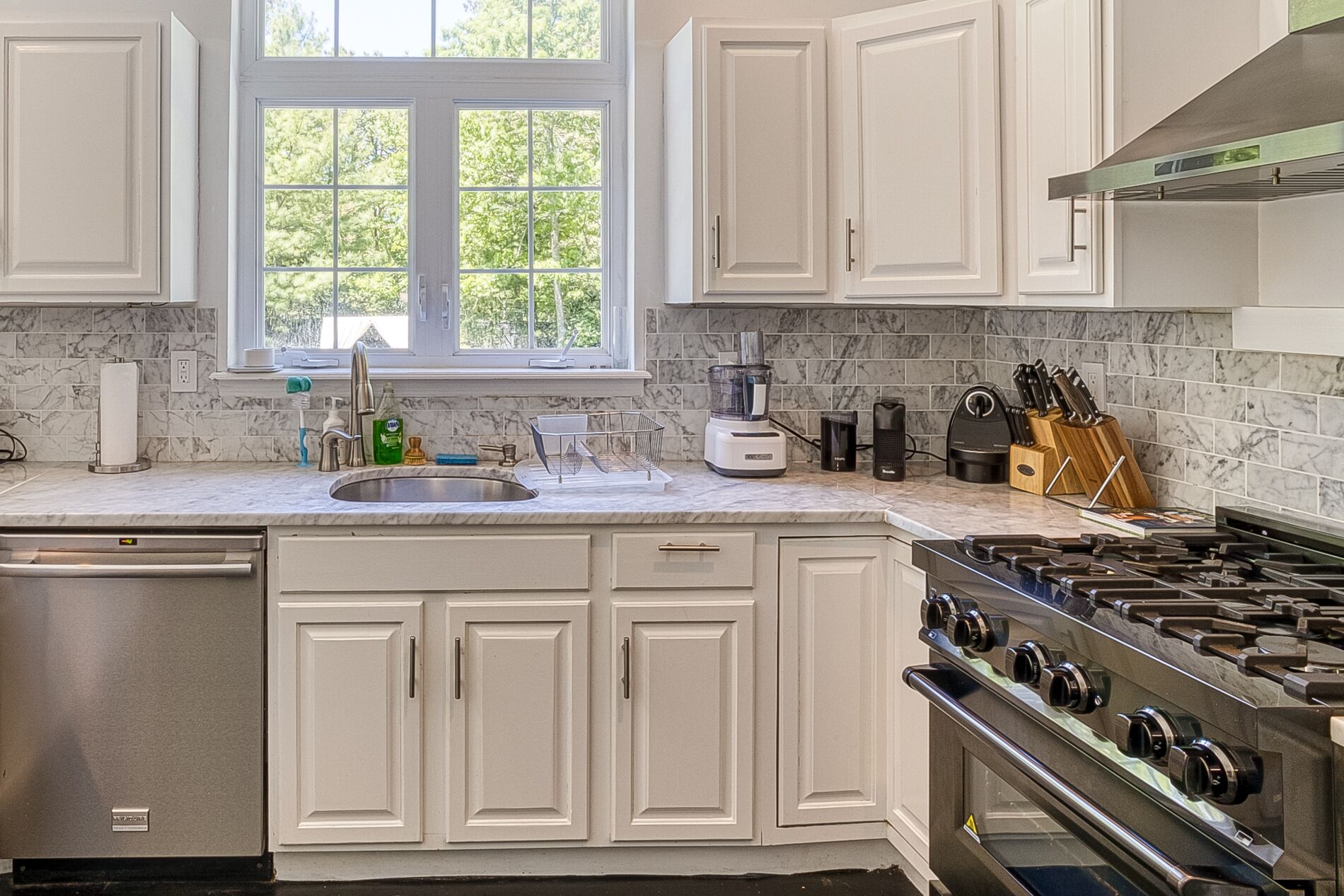 A kitchen with white cabinets, a built-in stove, and a window with a view of trees.