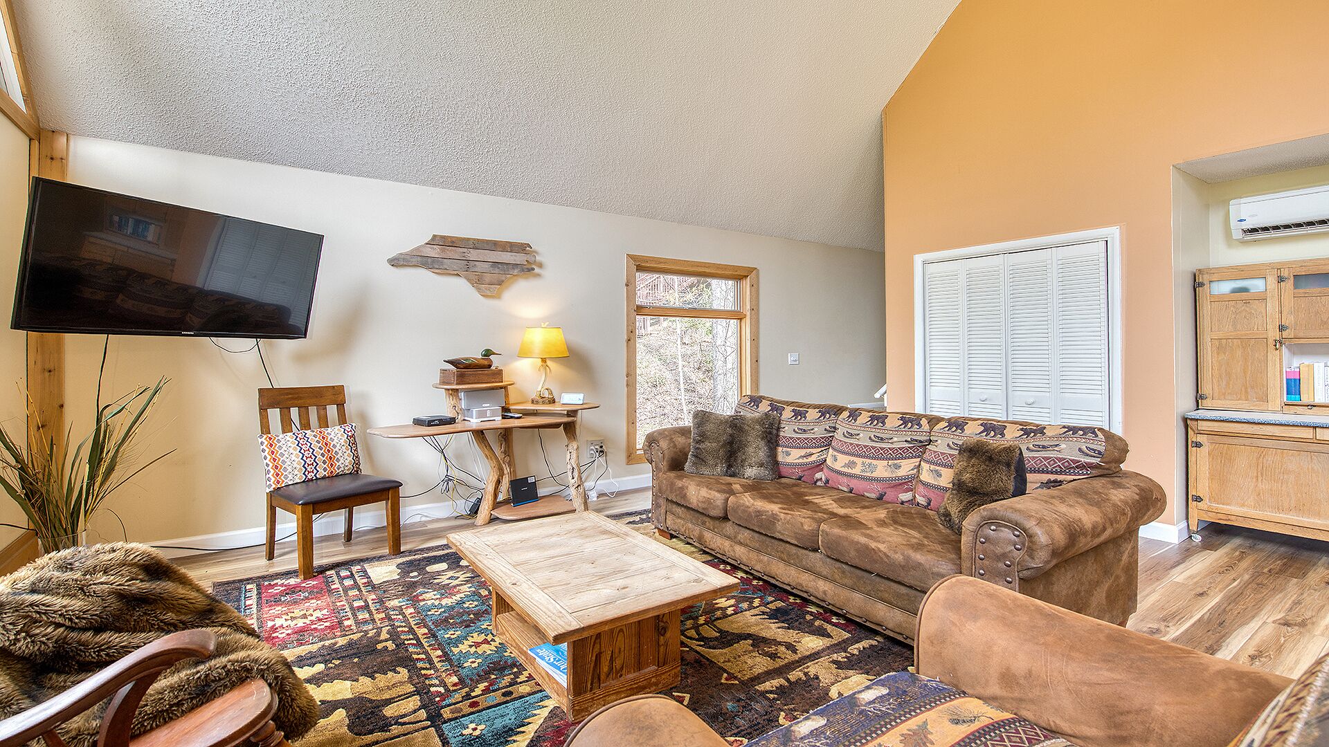 A cozy living room with a sofa, armchair, coffee table, and a flat-screen TV mounted on the wall.