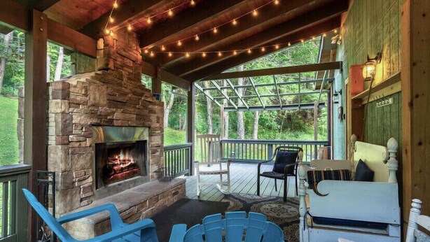 Une véranda couverte avec une cheminée en pierre, des fauteuils Adirondack bleus et un banc en bois.