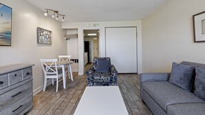 Un espace de vie compact comprenant une table et des chaises, un fauteuil à motifs, un canapé gris et une commode blanche.