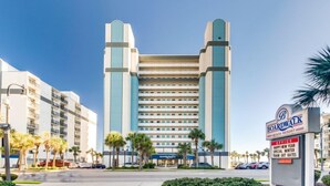 Un grand hôtel moderne, doté d’une tour centrale remarquable et d’une enseigne indiquant qu’il s’agit d’un complexe hôtelier situé sur la promenade de bord de mer.