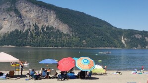 A beach with people, colorful umbrellas, and a mountain in the background. - 4 Bedroom Home in the Shuswap,  Close to Canoe Beach! (Canoe)
