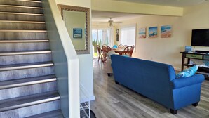 A staircase with a wooden finish, a blue sofa with patterned cushions, and a dining area with wooden chairs and a table. - 4 Bedroom Home in the Shuswap,  Close to Canoe Beach! (Canoe)