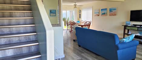 A staircase with a wooden finish, a blue sofa with patterned cushions, and a dining area with wooden chairs and a table.