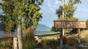 A wooden sign with the text "Canoe Beach Boat Launch" surrounded by natural scenery and a body of water. - 4 Bedroom Home in the Shuswap,  Close to Canoe Beach! (Canoe)