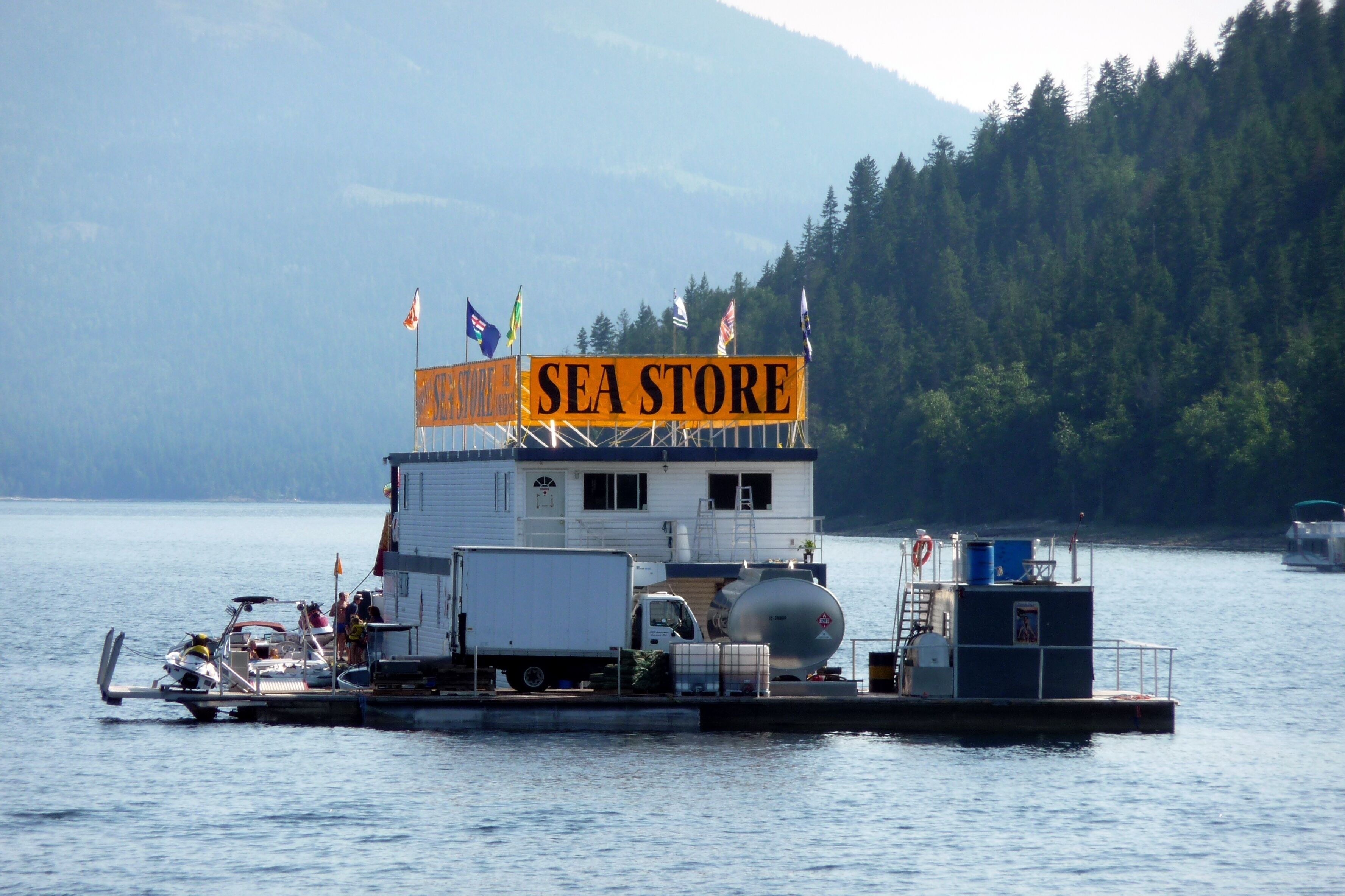A ferry with a 'SEA STORE' sign, docked at a pier with a forested mountain backdrop.
