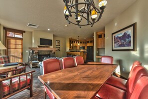 A dining area with a wooden table and red upholstered chairs, a stone fireplace, and a kitchen with wooden cabinets and a refrigerator. - 2BR Ski-in-Out Condo with Pool (Park City)