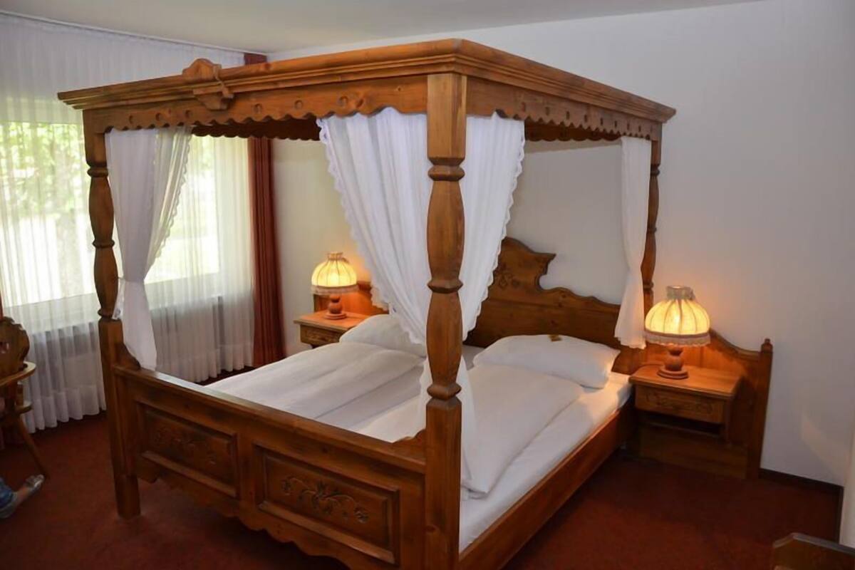 A four-poster bed with white linens, two bedside lamps, and a wooden nightstand.