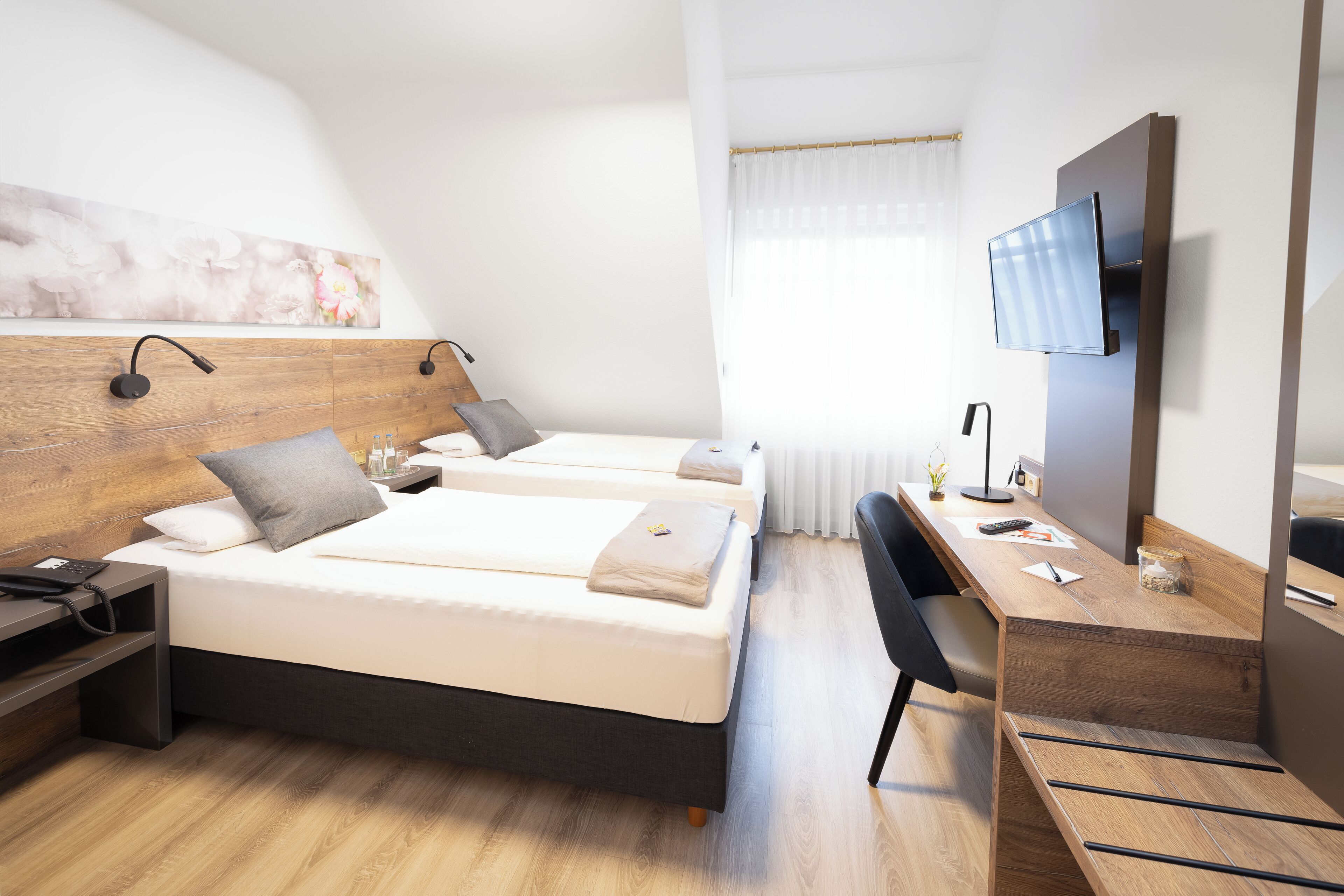 Una habitación de hotel moderna con dos camas, un escritorio, un televisor y un ventanal con cortinas.