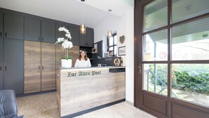 Una recepción con un letrero que dice "Zur Alten Post" en un interior moderno con armarios de madera y un ventanal grande.