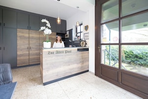 Una recepción con un letrero que dice "Zur Alten Post" en un interior moderno con armarios de madera y un ventanal grande.