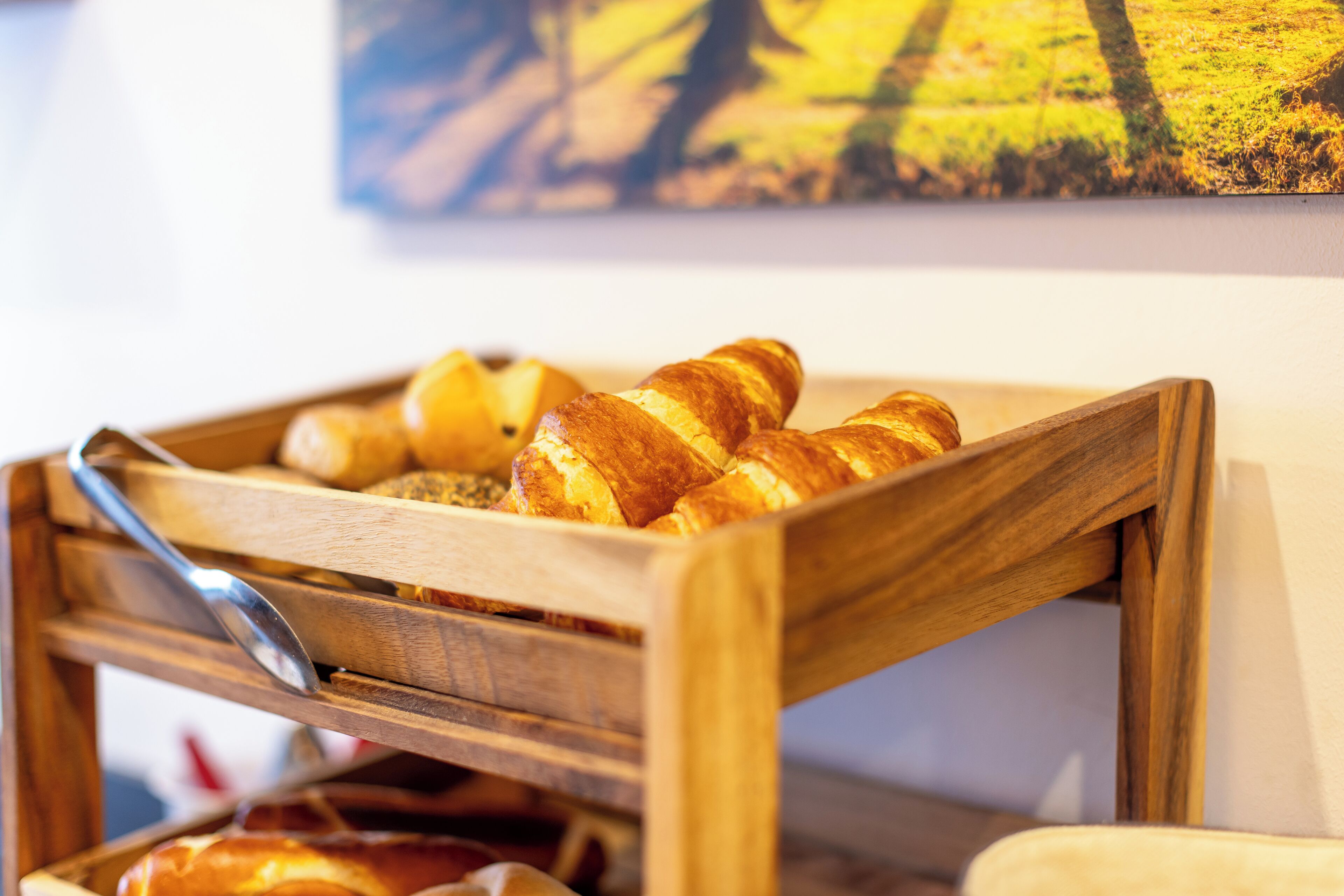 Una cesta de madera con cruasanes y una baguette sobre una mesa.