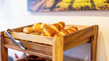 Una cesta de madera con cruasanes y una baguette sobre una mesa.