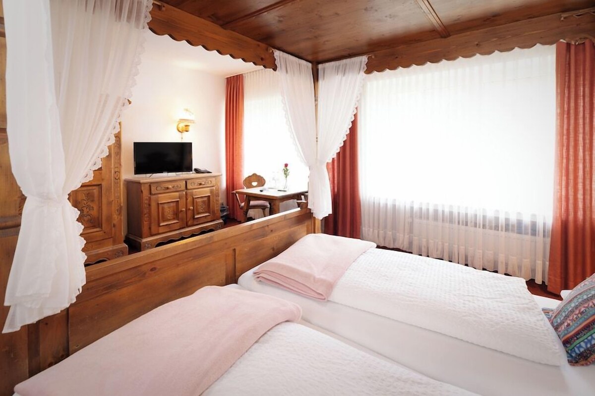 A room with a bed, a TV, a wooden dresser, and a desk with a chair.