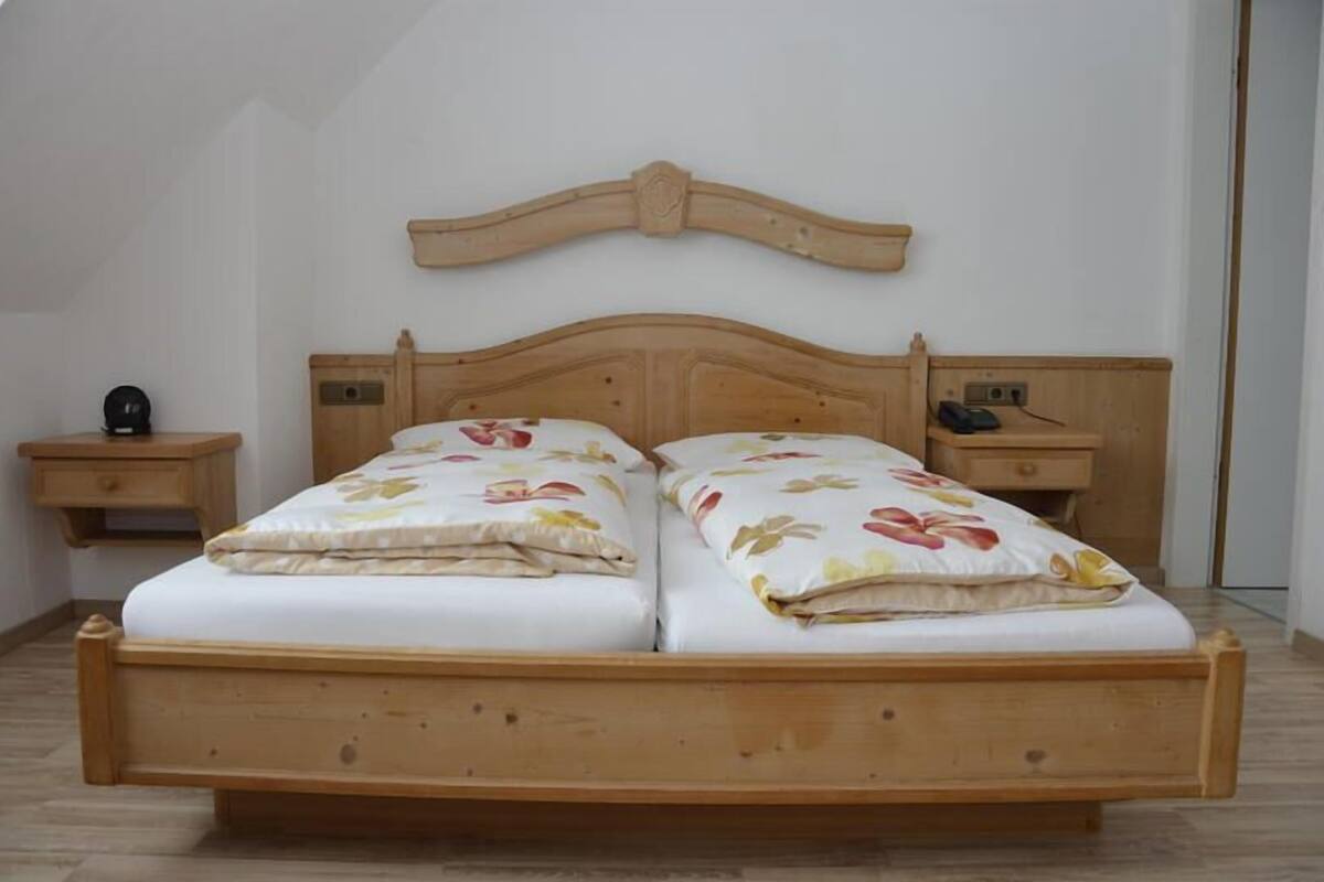 A double bed with floral bedding, wooden headboard, bedside tables with lamps, and a wooden floor.