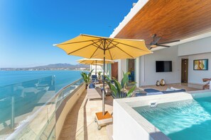 A poolside area with a view of the sea, outdoor seating, and a ceiling fan.