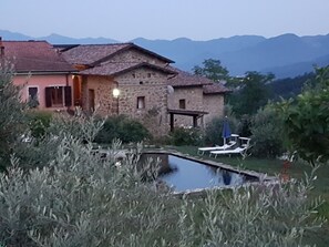 Una casa de piedra con piscina y sillas de descanso, rodeada de montañas.