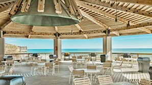 An outdoor patio with wooden tables and chairs, overlooking the ocean.