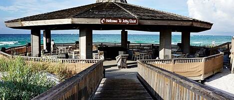 Un muelle de madera que lleva a un pabellón cubierto con un cartel que dice 'Welcome to Jetty East', con vista al océano.