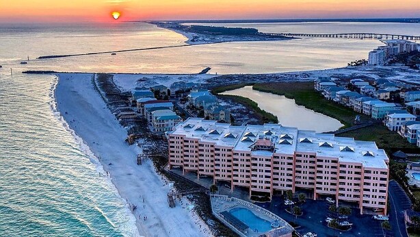 A coastal hotel with a beachfront, a swimming pool, and a pier in the background.