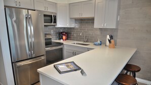 A modern kitchen with stainless steel appliances, a built-in oven, and a large island with stools.