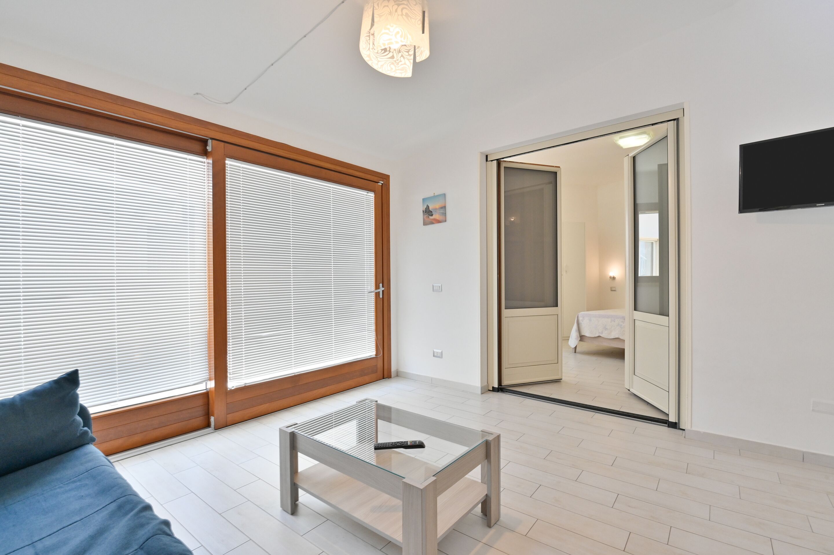 Een moderne kamer met een bank, een glazen salontafel, een schuifdeur naar een badkamer en een tv aan de muur.