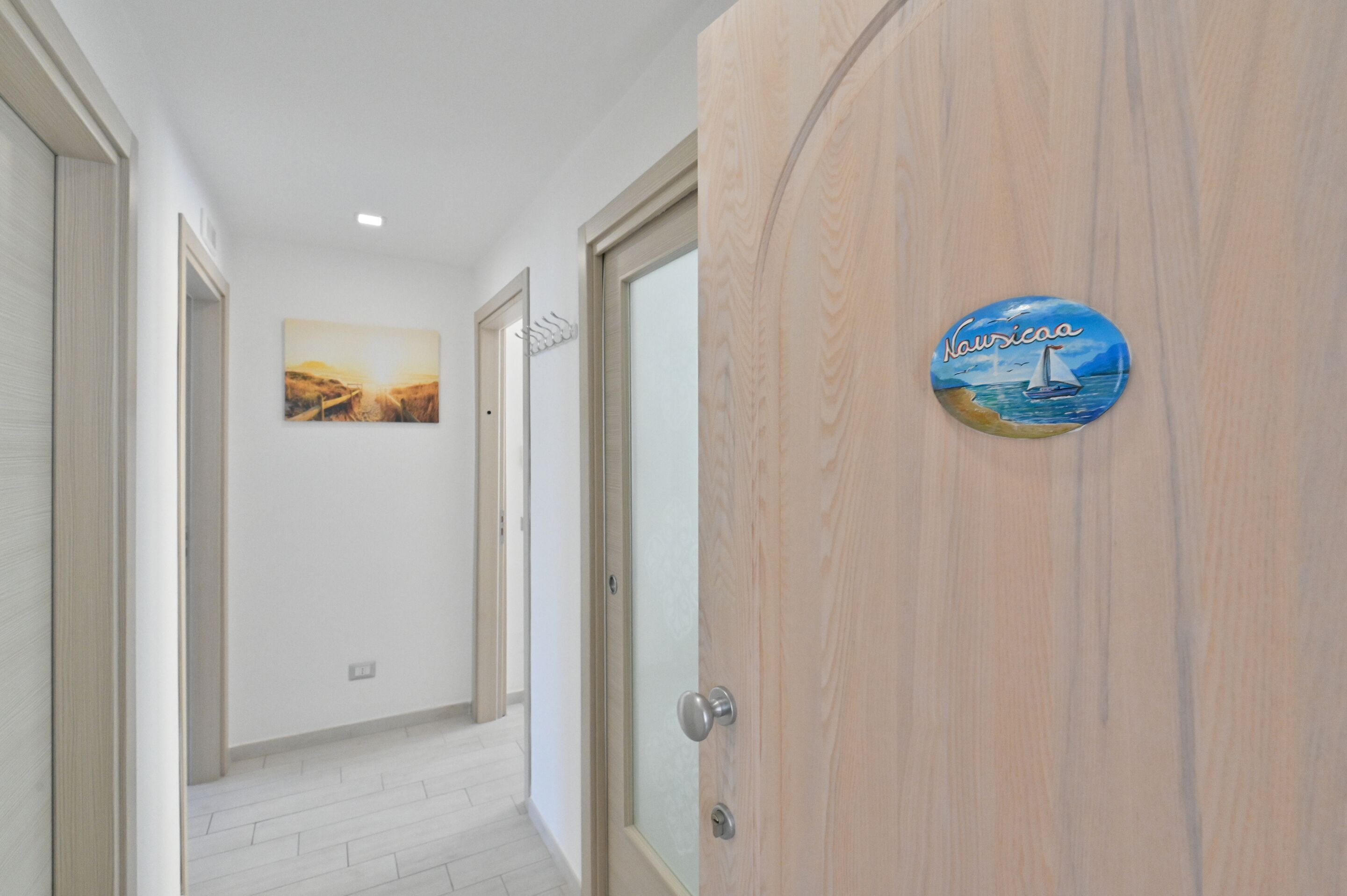 Un pasillo con una puerta de madera, un cuadro enmarcado en la pared y un letrero con un velero.