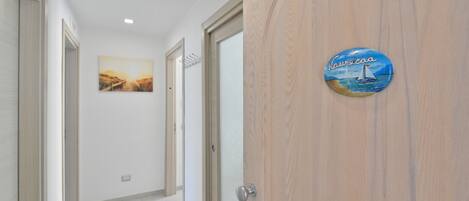 Un pasillo con una puerta de madera, un cuadro enmarcado en la pared y un letrero con un velero.