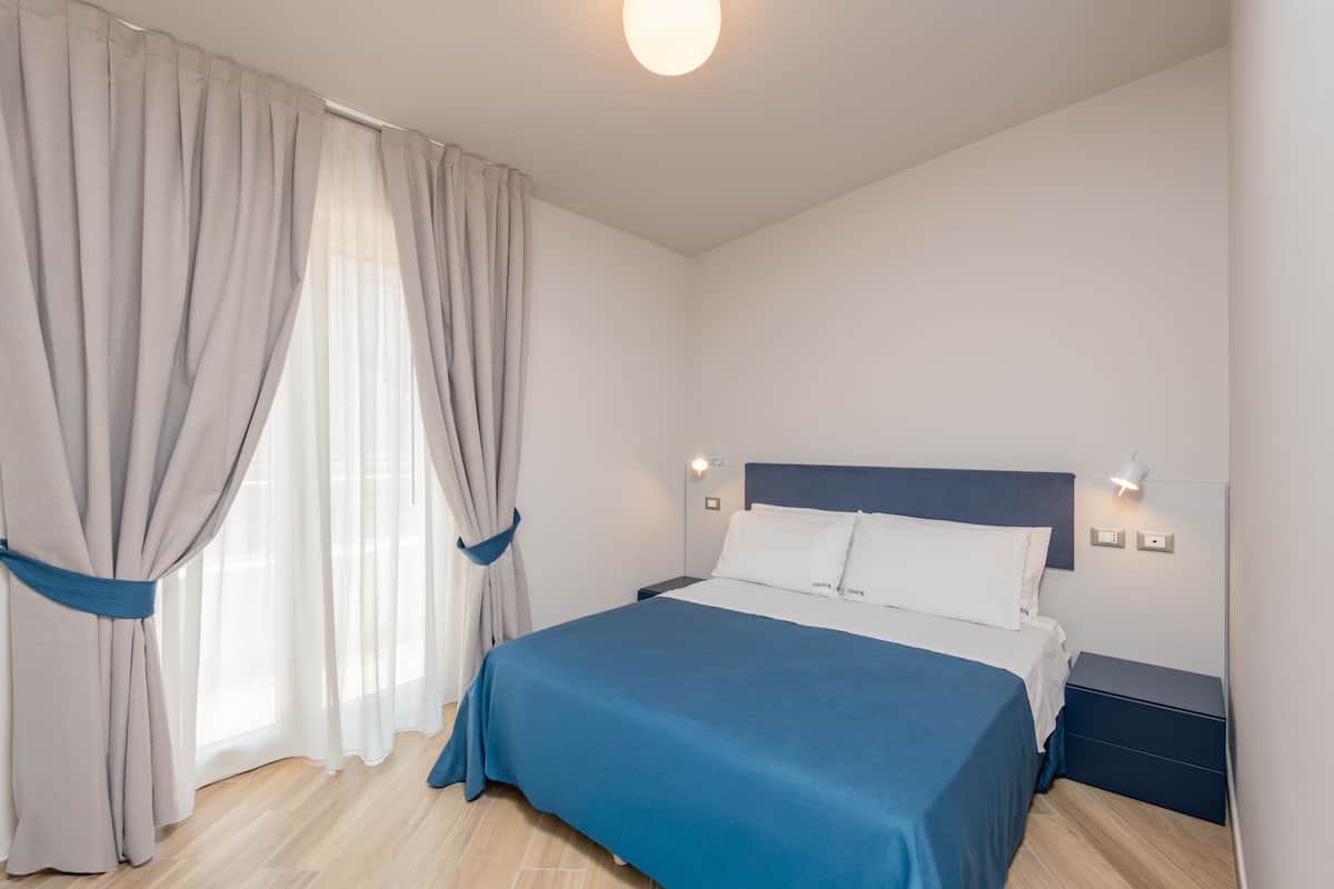 Ein Schlafzimmer mit einem Bett, Vorhängen, Nachttischen und einer Wandleuchte.