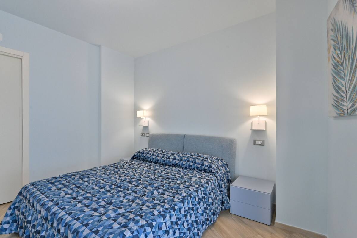Ein Schlafzimmer mit Bett, Nachttischlampen, einem Nachttisch und einer Wandleuchte.