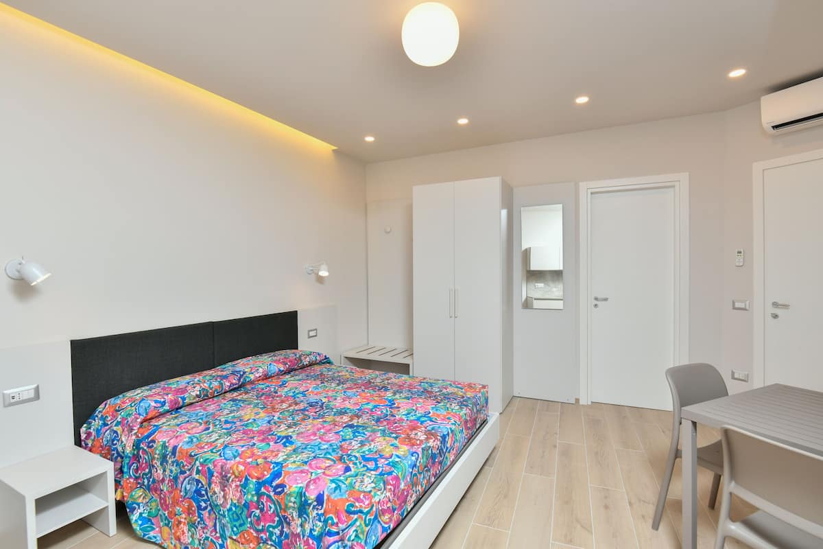 Ein modernes Schlafzimmer mit einem Bett, einem Schreibtisch und einem Stuhl. Weiße Schränke und eine Tür mit Spiegel.