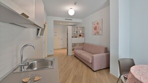 A modern kitchen with a sink, a dining area with a table and chairs, a sofa, and a bookshelf. - Odissea Residence e Rooms (Castellabate)