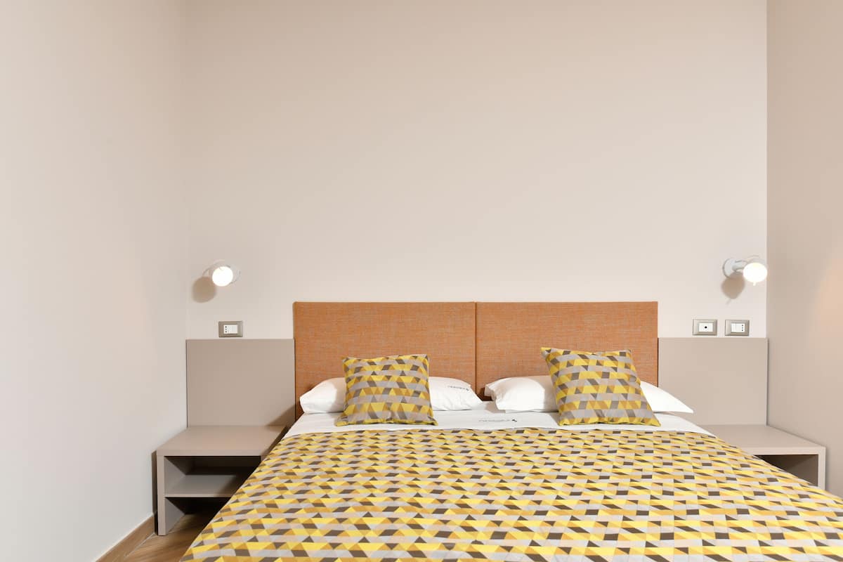 Ein modernes Hotelzimmer mit einem aufgeräumten Bett, zwei Nachttischen und einem Kopfteil mit integrierter Beleuchtung.