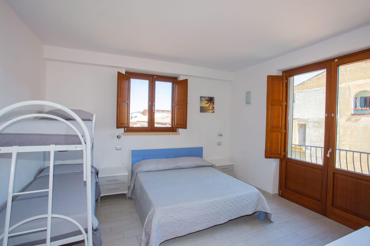 A bedroom with a bunk bed, a single bed, a window with a view, and a wooden door.