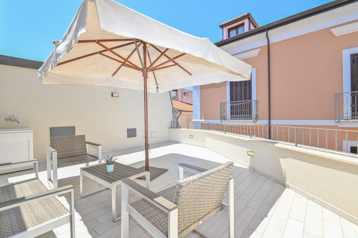 Eine Dachterrasse mit Gartenmöbeln, einem Tisch und einem großen Sonnenschirm.