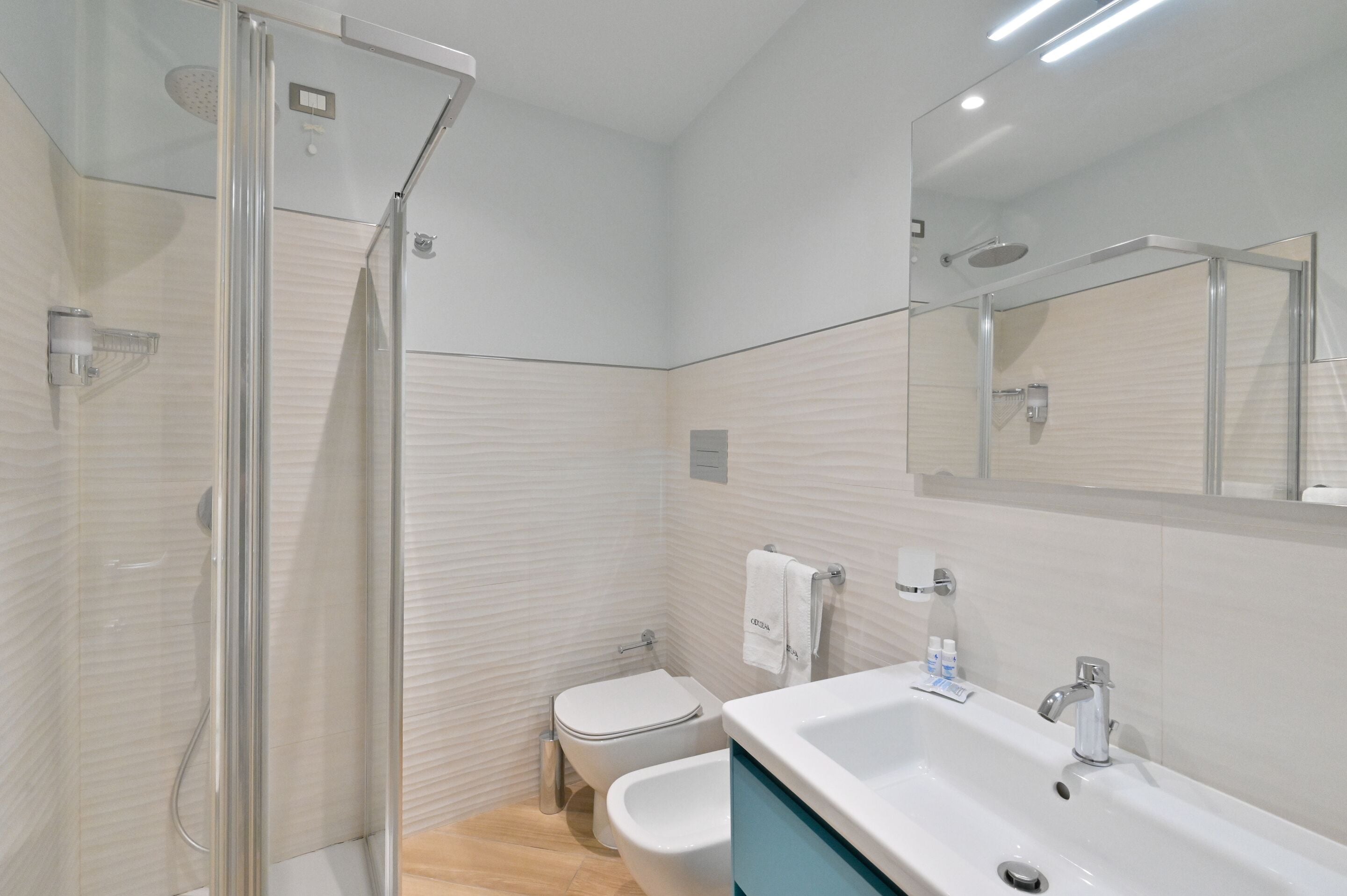 A modern bathroom with a glass-enclosed shower, a white toilet, a bidet, and a large sink with a mirror above.