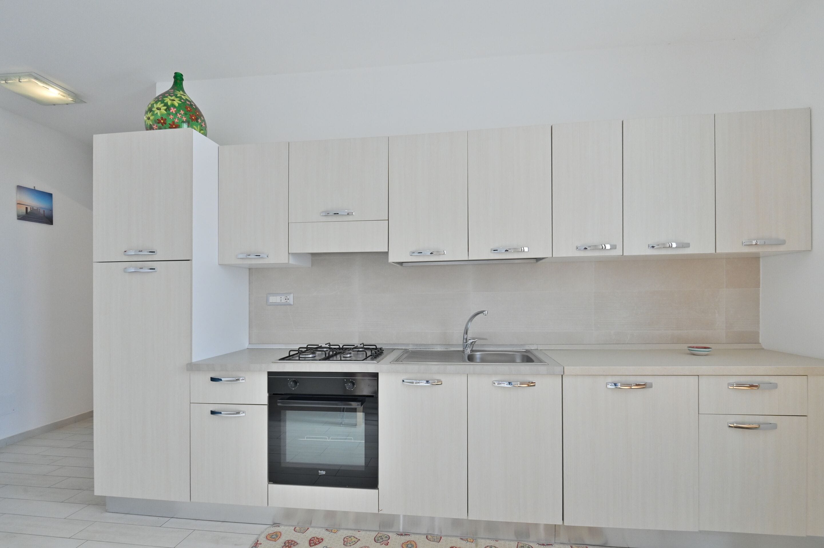 A modern kitchen with light wood cabinets, a built-in oven, and a gas stove.