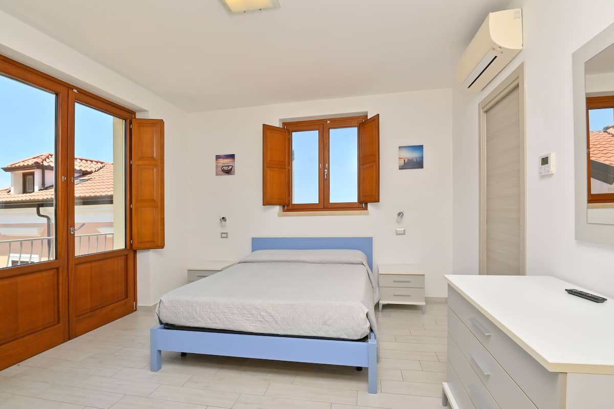 Ein Schlafzimmer mit Bett, Schreibtisch, Kleiderschrank, Fenster und Klimaanlage.