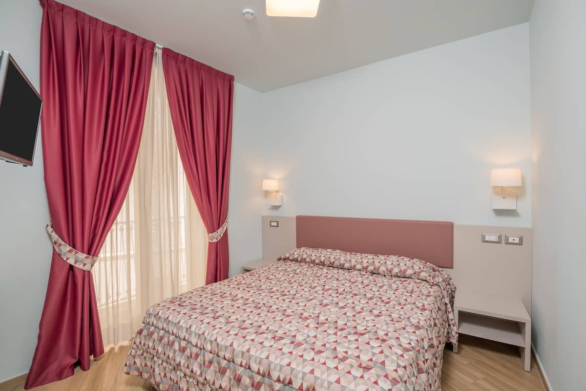 Ein Schlafzimmer mit Bett, Vorhängen, Wandleuchten und einem Fernseher.