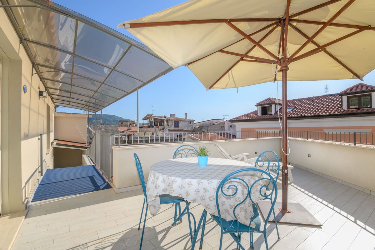 Eine Dachterrasse mit Tisch, Stühlen, einem großen Sonnenschirm und einem Blumentopf.