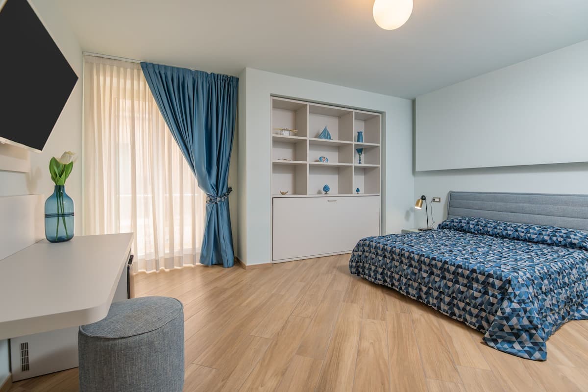 Ein modernes Schlafzimmer mit Bett, Schreibtisch, Stuhl, Kleiderschrank und Fernseher.