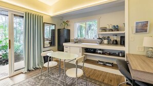 A compact kitchen with a dining area, a refrigerator, a sink, and a window with a view of greenery. - NEW! PonoMana Oasis - The Koi Cottage (Captain Cook)