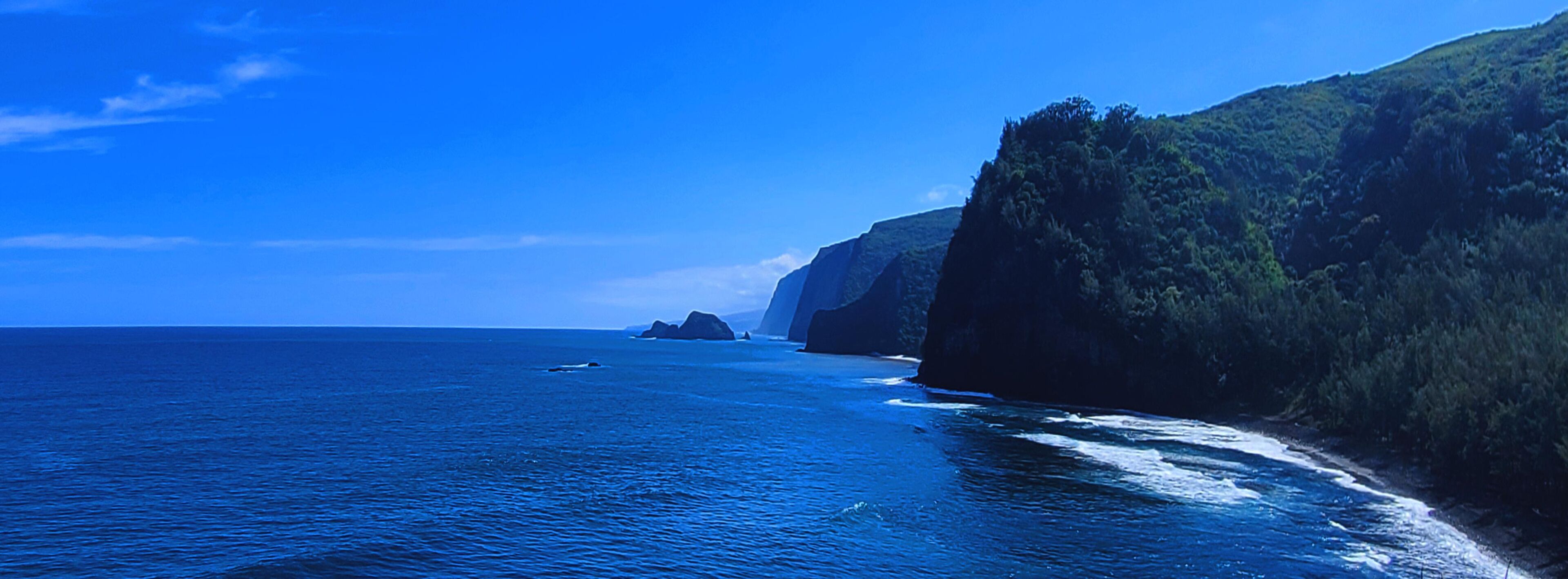 Eine Küstenlandschaft mit blauem Meer, schroffen Klippen und einer entfernten Insel.