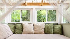 A bedroom with a large bed, three windows, and a view of greenery. - NEW! PonoMana Oasis - The Koi Cottage (Captain Cook)