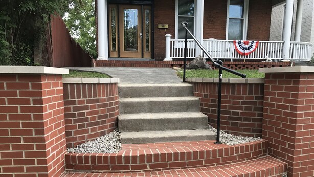 Un conjunto de escalones exteriores que conducen a la entrada de un edificio, con una barandilla blanca y una bandera decorativa.